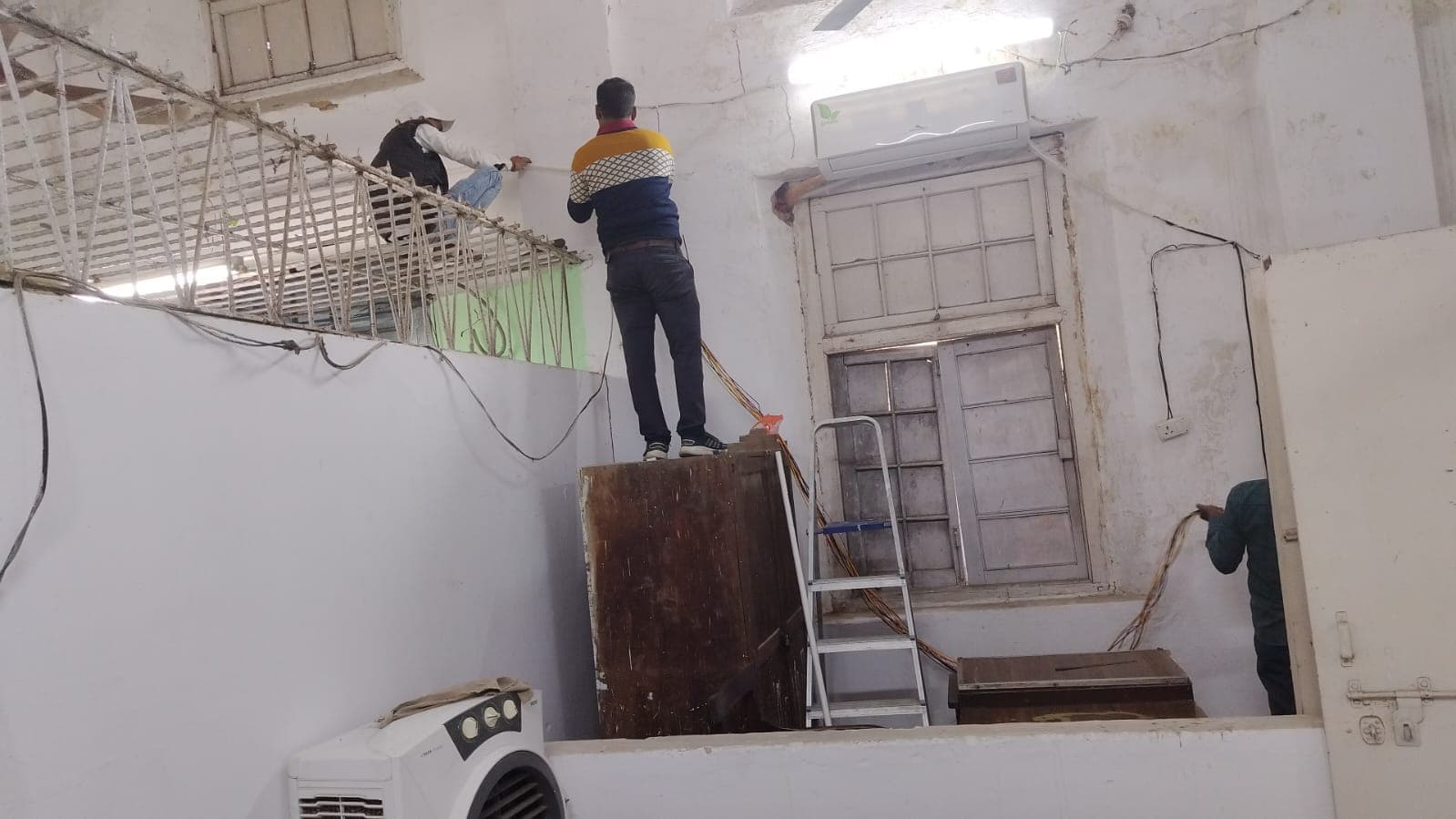 Electricians running conduit and cable at high level inside an office hall