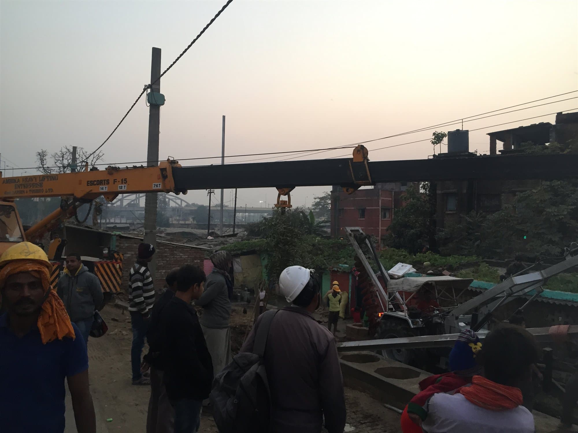 Crew in hard hats guiding a steel section down from a crane hook at first light