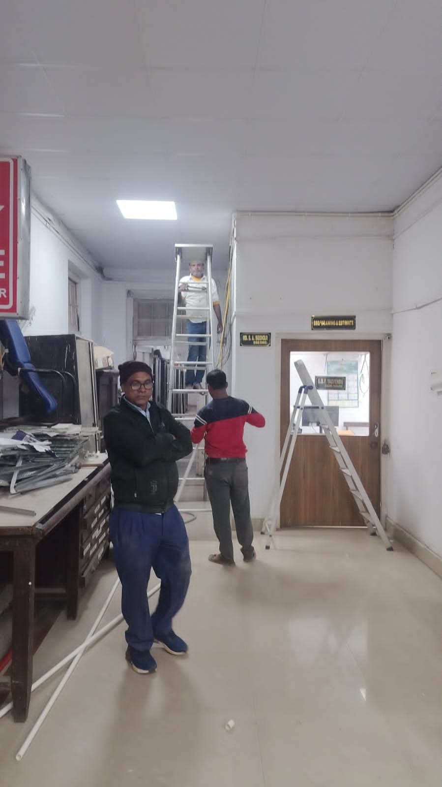 Electricians on ladders installing conduit along an office corridor