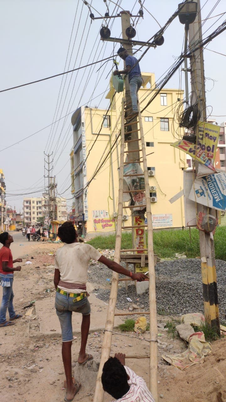 A lineman working at the top of a street pole from a bamboo ladder
